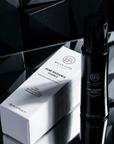 Black and white Bella Aura skincare product on a reflective surface with geometric background