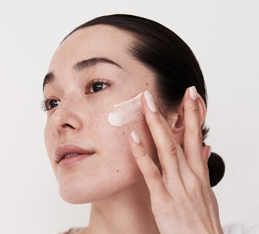 woman applying bella aura skincare cream on a white background