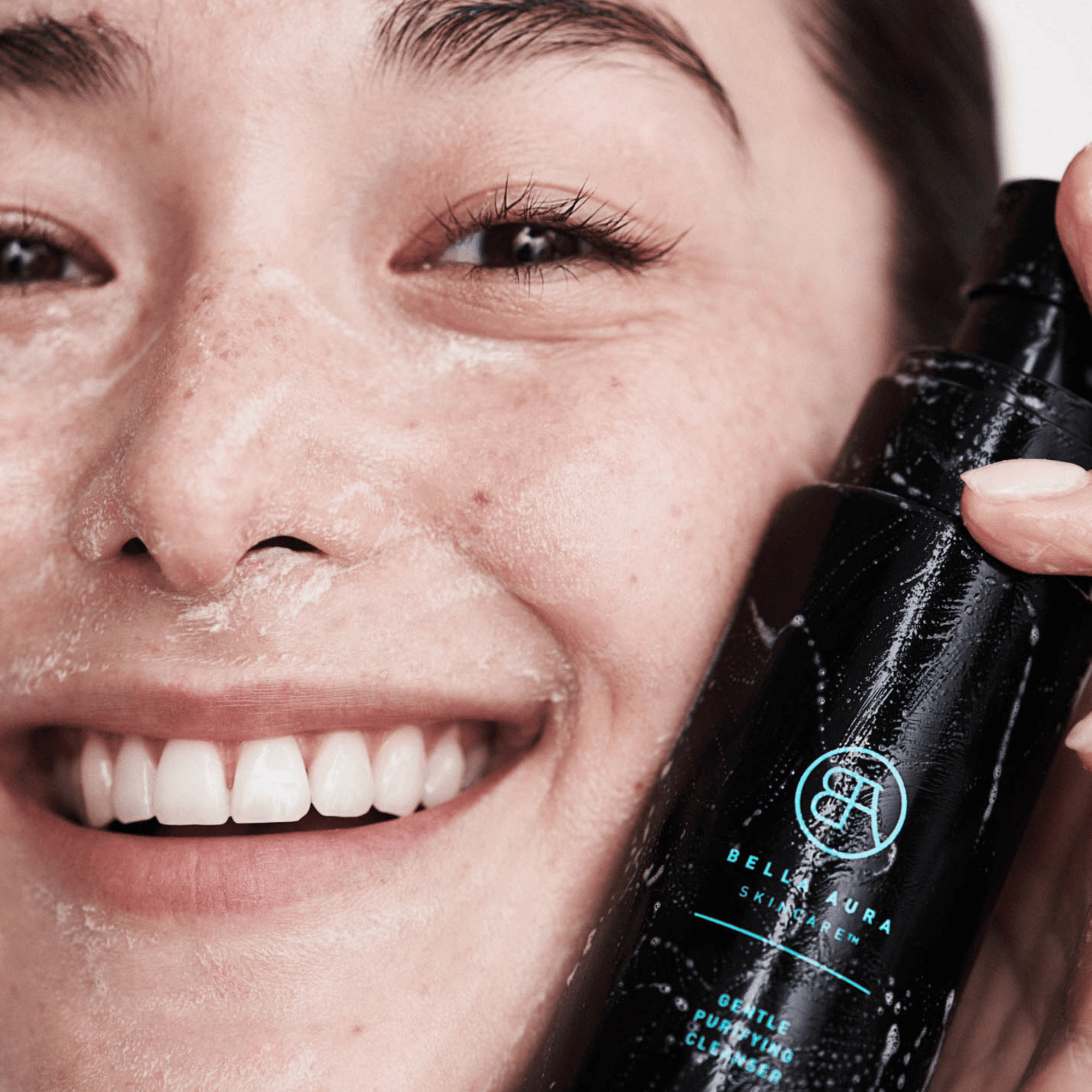 woman holding a black bottle labeled &#39;Bella Aura cleanser&#39; near their face.