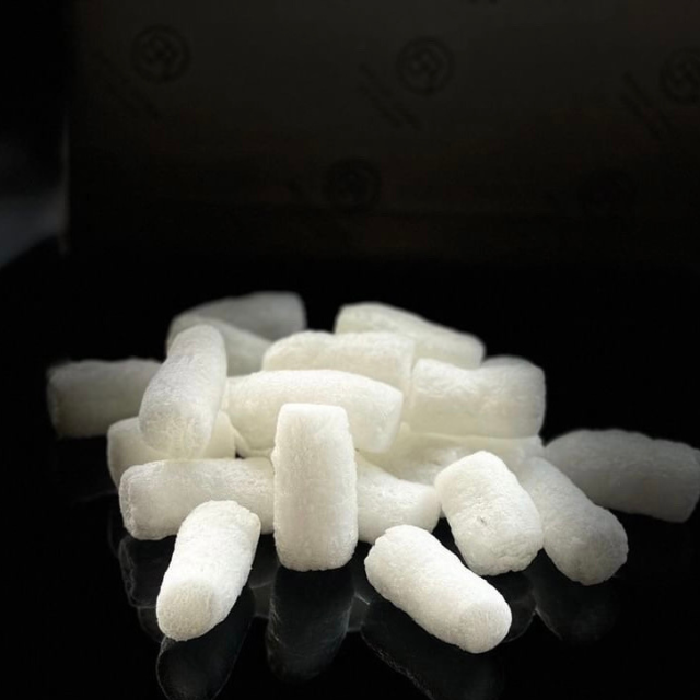 A pile of white biodegradable packaging peanuts, representing Bella Aura's eco-friendly packaging choice.
